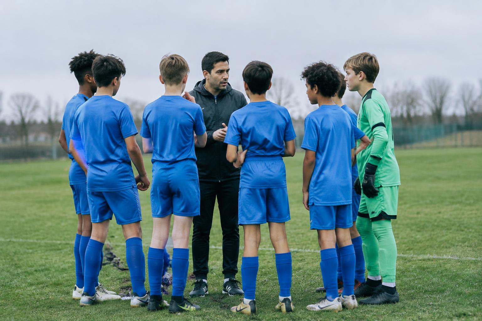 Squadra di calcio giovanile in cerchio con l'allenatore durante un briefing a bordo campo